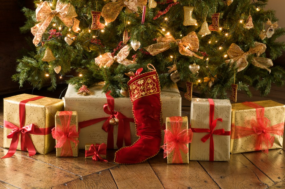 Christmas presents in gold and red gift wrap under a traditional Christmas tree with a red stocking.