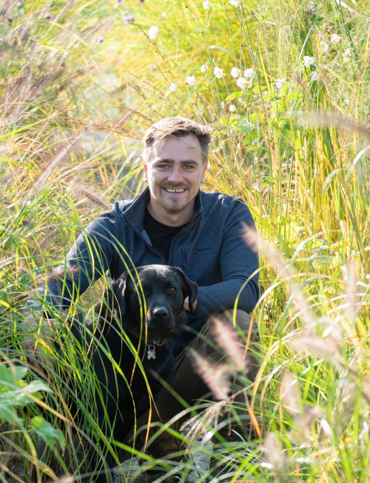 Man and black dog sitting in tall grass.