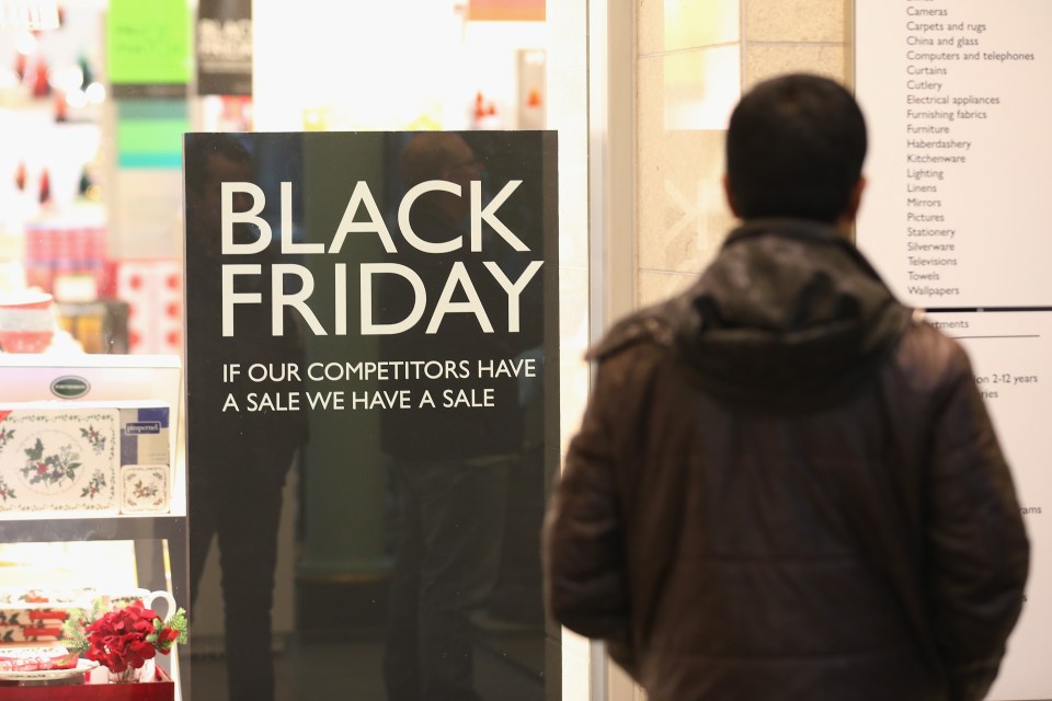 A person looking at a "Black Friday" sign that reads "If our competitors have a sale we have a sale" in a store window.
