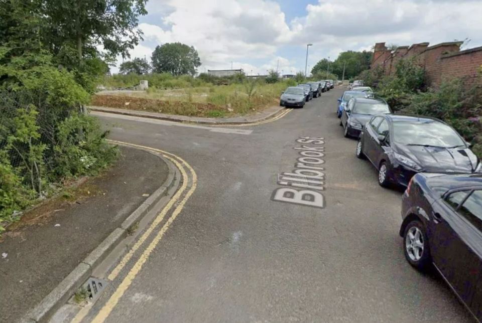 A street corner where Bilbrook Street is written on the road, with cars parked along the curb and an undeveloped, overgrown lot across the street.