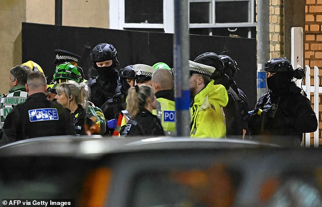 Armed Police officers stand with members of the emergency services outside Huntingdon station