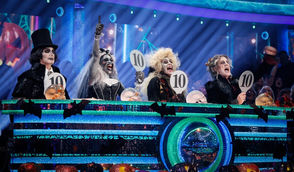 Craig Revel Horwood, Motsi Mabuse, Shirley Ballas, and Anton Du Beke dressed in Halloween costumes as judges on Strictly Come Dancing, all holding up signs with the number 10.