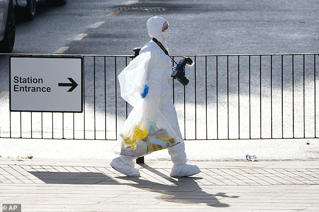 A forensic investigator pictured carrying a bag full of evidence on Sunday morning as investigations continue