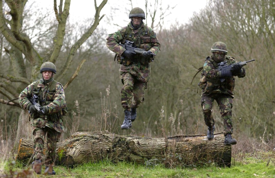 Three members of the British 16 Air Assault Brigade train, with two soldiers jumping over a log.