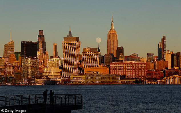 The Beaver Moon rises behind the Chrysler Building and the Empire State Building as the sun sets in New York City on November 4, 2025, as seen from Hoboken, New Jersey