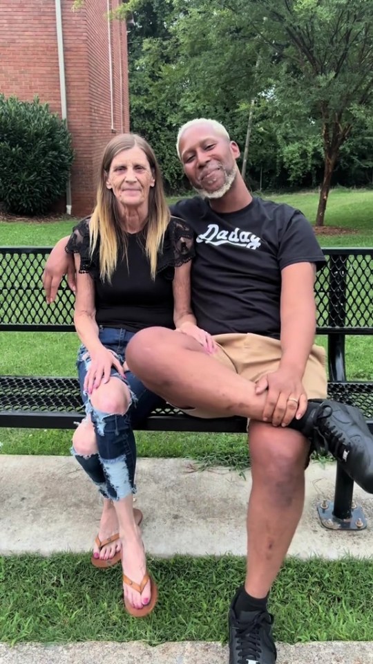 A woman in ripped jeans and a man in shorts sitting on a bench with their arms around each other.