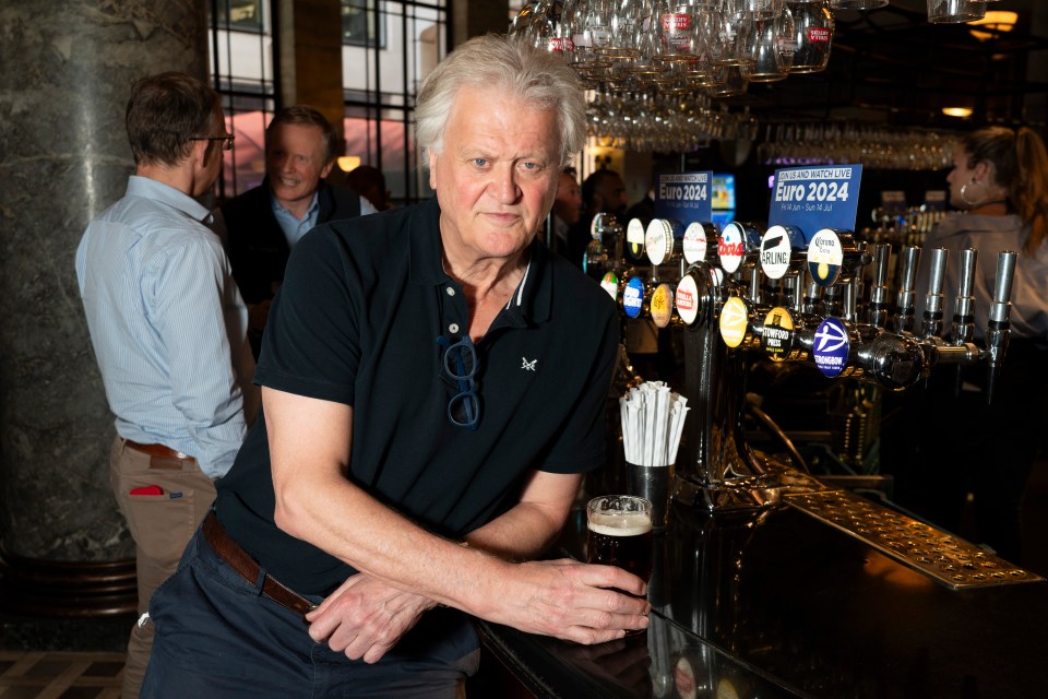Tim Martin leaning on a bar with a pint of beer in hand, surrounded by beer taps and a "Euro 2024" sign.