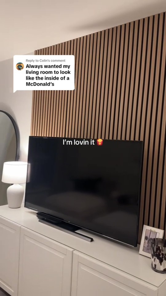 A white TV stand with a TV on it, with a wood-slat wall behind it, and a text overlay that reads "Always wanted my living room to look like the inside of a McDonald's" and "I'm lovin it" with a french fries emoji.