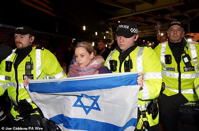 A woman holding an Israeli flag gets dragged away by police officers as tempers flare ahead of Thursday's match