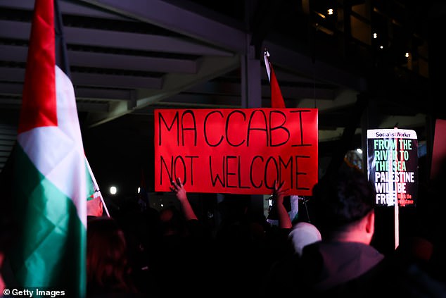 Demonstrators wave placards opposing Maccabi's involvement in the match and the arrival of their fans