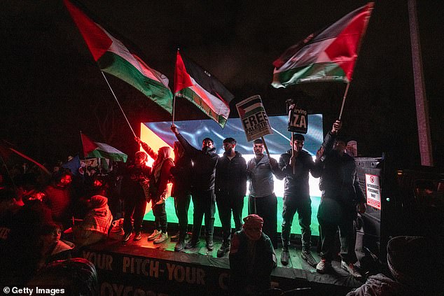 A row of demonstrators wave Palestinian flags in front of a screen
