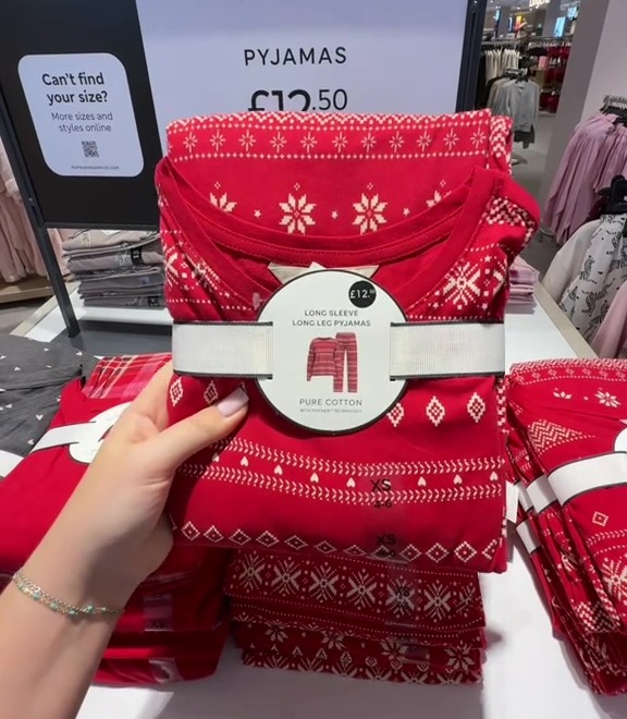 A hand holding a red pyjama set with white snowflake patterns and a label displaying "Pyjamas £12.50".