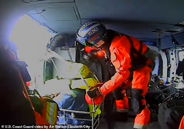 Video from the Defense Visual Information Distribution Service shows helicopter crews hoisting a sailor into the air while he sat in a metal rescue basket, wearing a life vest and soaked water gear (pictured)