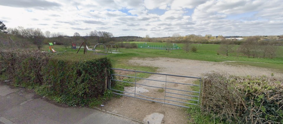 An open metal gate leading to a playground and sports fields.