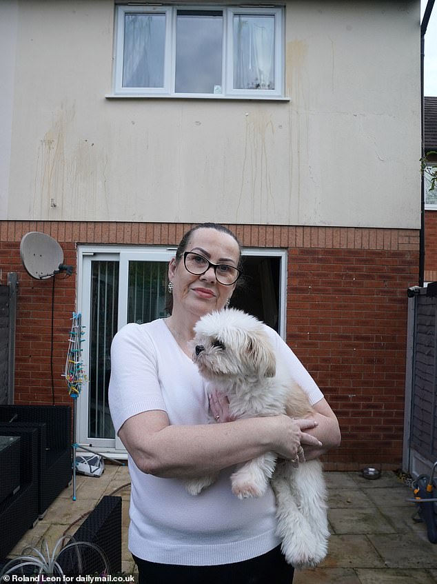 Celine stands in the garden with her dog, with egg and tomato stains running down her house