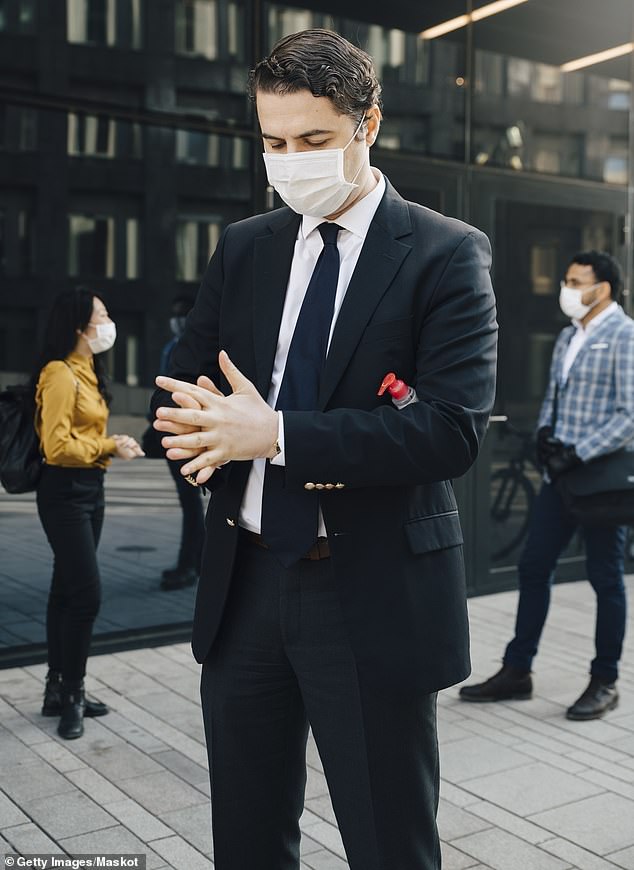 A businessman wearing a mask applies hand sanitiser during the Covid pandemic