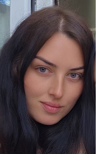 A woman with dark hair and blue eyes looking forward.