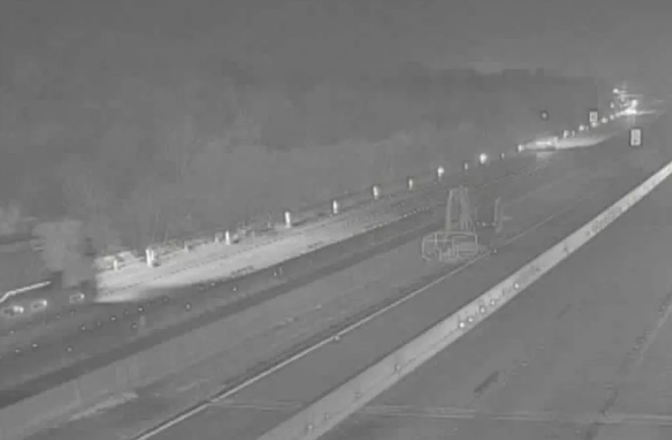 A multi-lane highway at night with a large vehicle on the left emitting smoke.