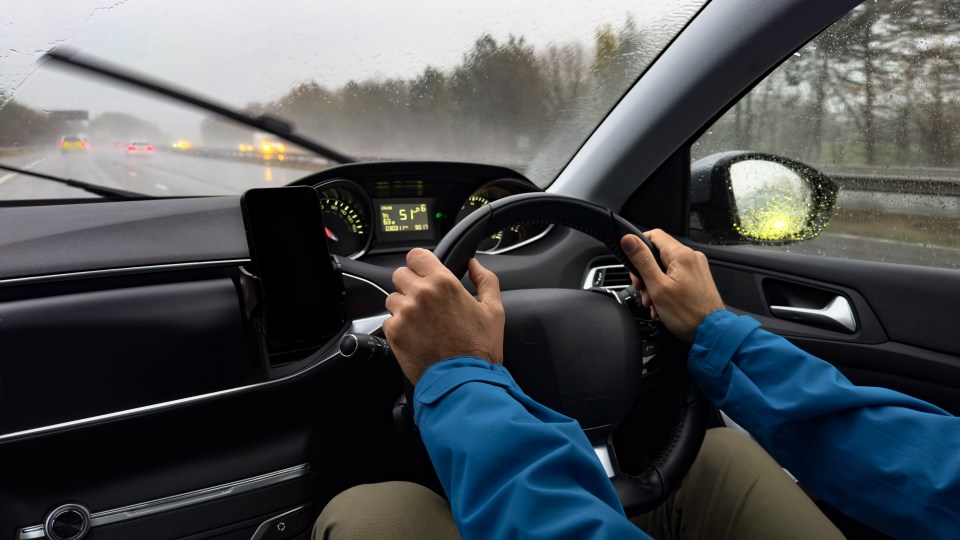 Man driving a right-hand-drive car on a rainy day.