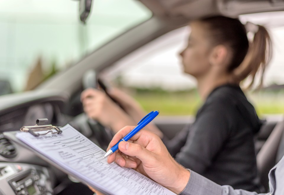 A driving instructor marking a checklist on a clipboard next to a teenage girl driving.