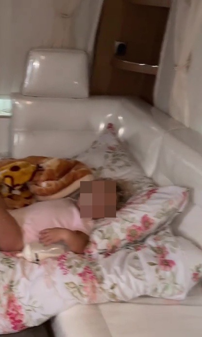 A child asleep on a floral-patterned bed with a baby bottle on their stomach.