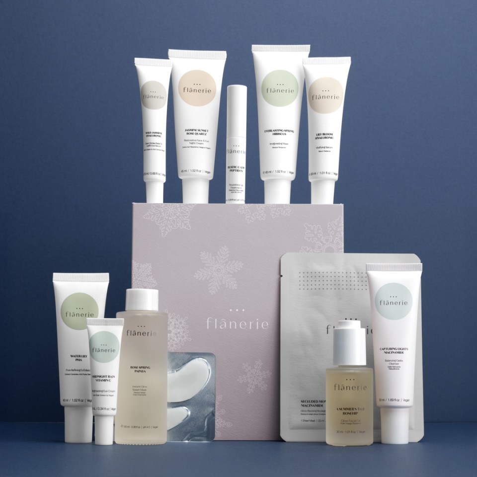 A collection of Flânerie skincare products, including tubes, bottles, an eye mask, and a sheet mask, arranged on and around a light purple box with snowflake illustrations.