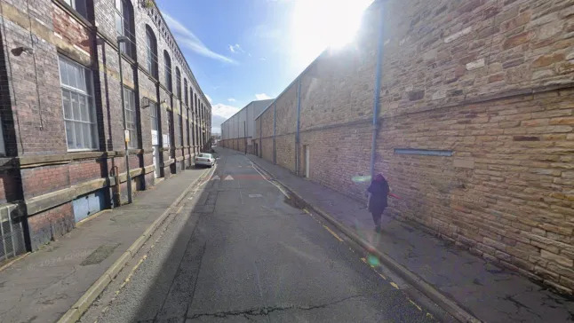 A person walking down an alleyway between two industrial buildings.