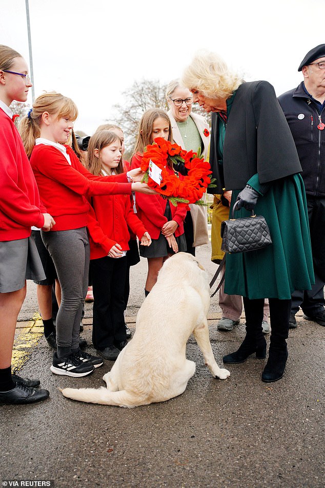 Queen Camilla is presented with a crocheted poppy wreath by Eira Jones, 10, at Chippenham train station