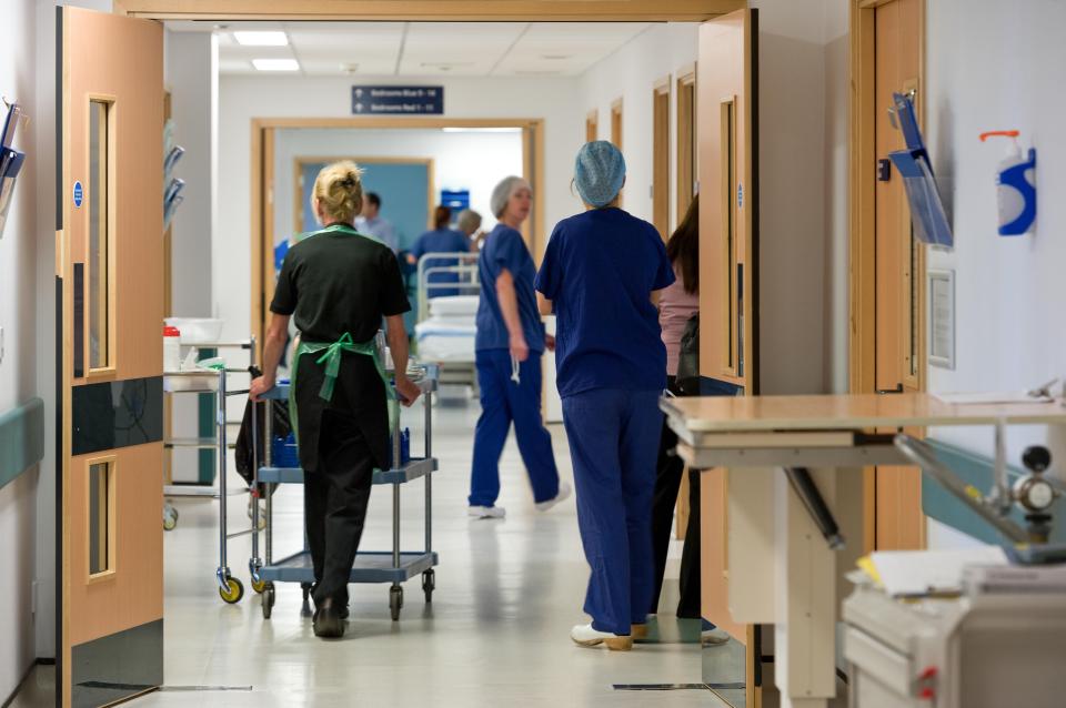 Healthcare personnel in an NHS hospital corridor.