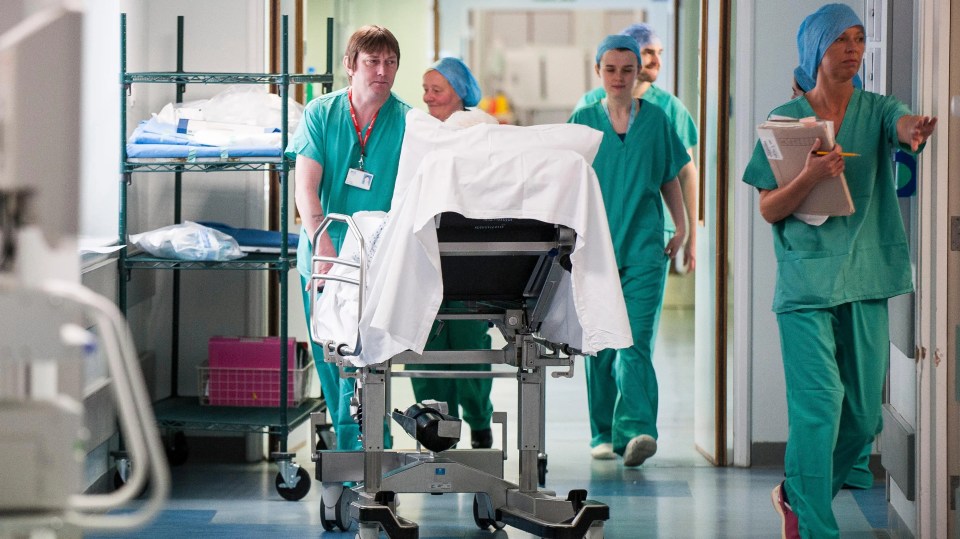 Medical staff moving a patient on a gurney through a hospital hallway.
