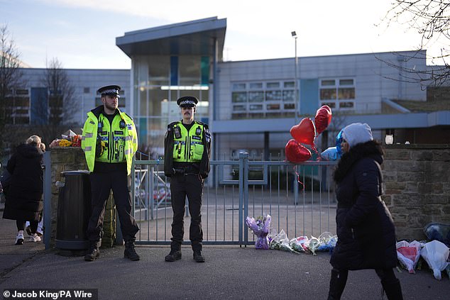 Police officers and floral tributes are seen outside All Saints Catholic High School where the murder took place