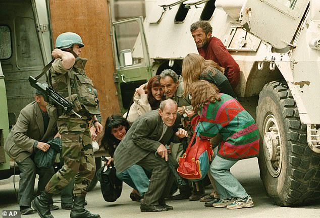 A French UN soldier stands alongside a group of Sarajevans seeking shelter behind a UN armoured personnel carrier from sniper-fire