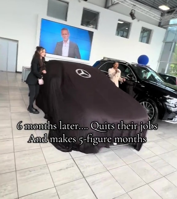 Two women in a car showroom, one next to a covered Mercedes car and another by an uncovered black SUV, with a man on a screen in the background.