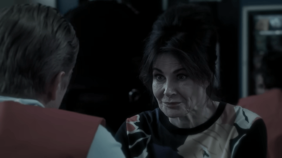 A woman in a floral shirt speaking to a person with their back to the camera.