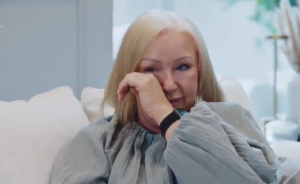 Woman with blonde hair crying while wiping her eye.