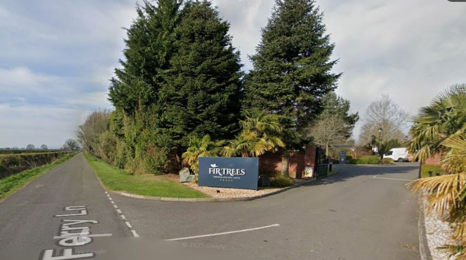 Roadside view of the entrance to Fir Trees hotel, showing a large sign, green trees, and the road "Ferry Ln" in the foreground.