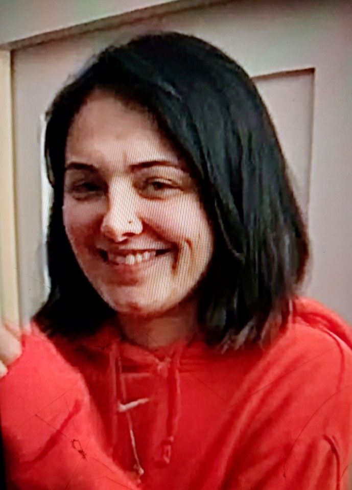 Headshot of Emily, a 27-year-old missing person, with shoulder-length black hair and a small scar on her right cheek, wearing a red hoodie, smiling.