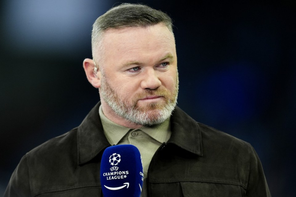 Wayne Rooney wearing a dark jacket and holding a microphone with the Champions League logo.