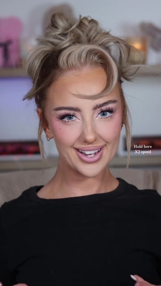 Woman with blonde hair pulled up, pink eyeshadow, and pink lipstick smiling at the camera.