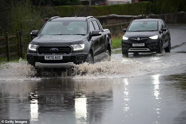 Vehicles are driven through a partially flooded road in Northwich, Cheshire, this afternoon
