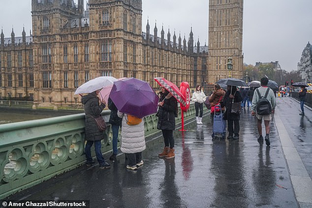 Pedestrians stand under umbrellas on Westminster Bridge today during a very wet morning