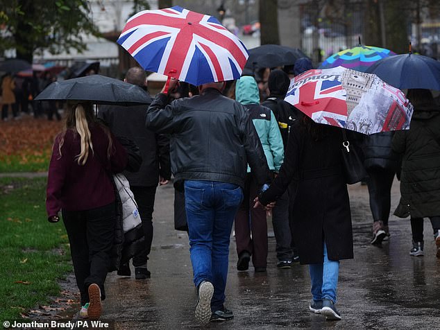 People shelter from the rain beneath Union Jack umbrellas in London's Green Park today