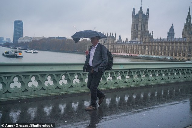 A pedestrian crossing Westminster Bridge with an umbrella during heavy rain this morning