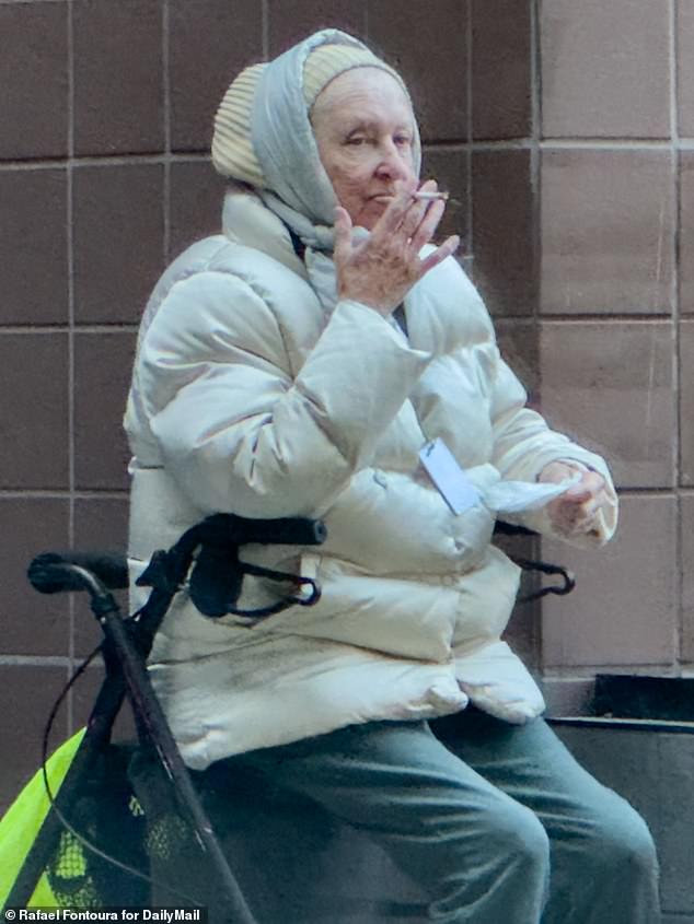 McKechnie in a puffa coat smoking a cigarette outside a high-rise affordable housing block for the elderly