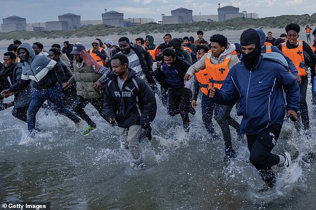 Migrants wade into the sea in an attempt to board a small boat on August 12, 2025 in Gravelines