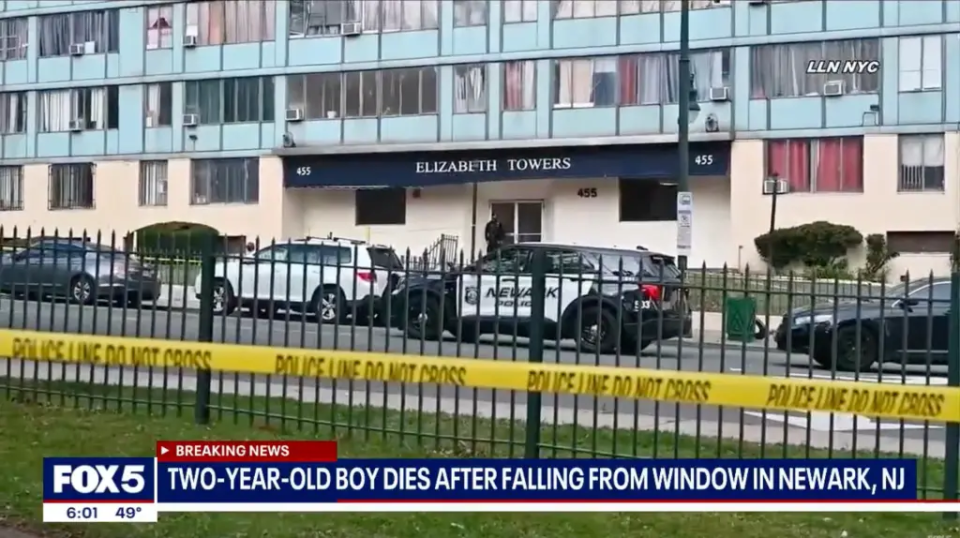 Police cars and crime scene tape outside Elizabeth Towers, with a news chyron about a child's death.