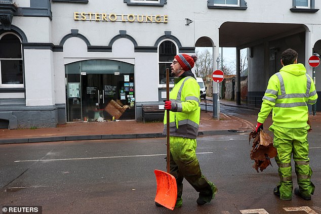 A man carries a shovel as a clean-up operation gets underway in Monmouth