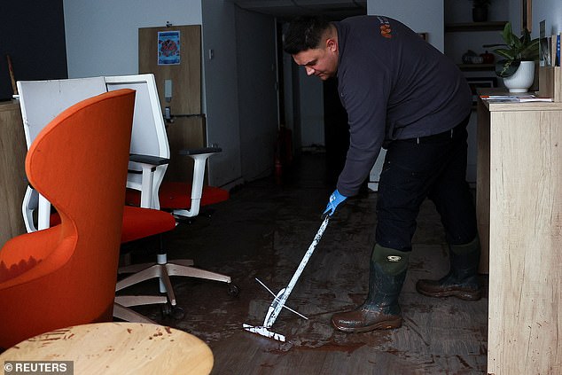 A man cleans inside his shop, following severe flooding caused by Storm Claudia, in Monmouth, Wales