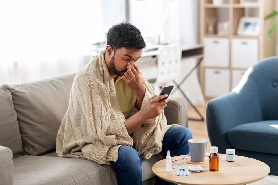 A sick young man in a blanket is on his smartphone at home.