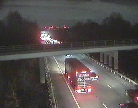 Overhead shot of traffic stopped on a highway at night with emergency vehicle lights in the distance.